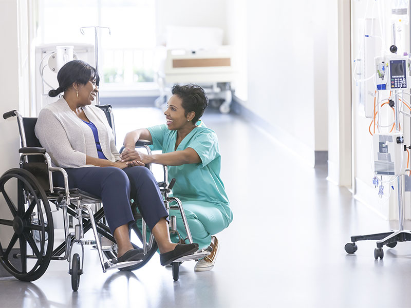 Female patient sitting on wheelchair and nurse having a happy conversation in the hospital
