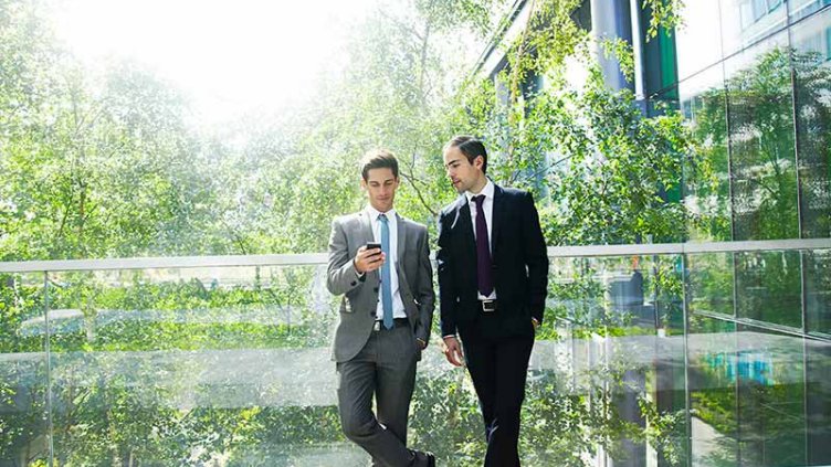 Two businessmen chatting surrounded by trees.