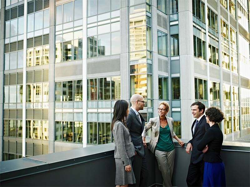 Group of coworkers standing in discussion on deck of office buildings in background