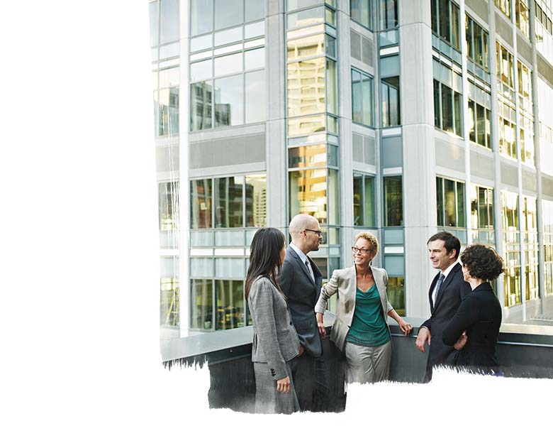 Tall glass office building with a group of five people standing in front talking