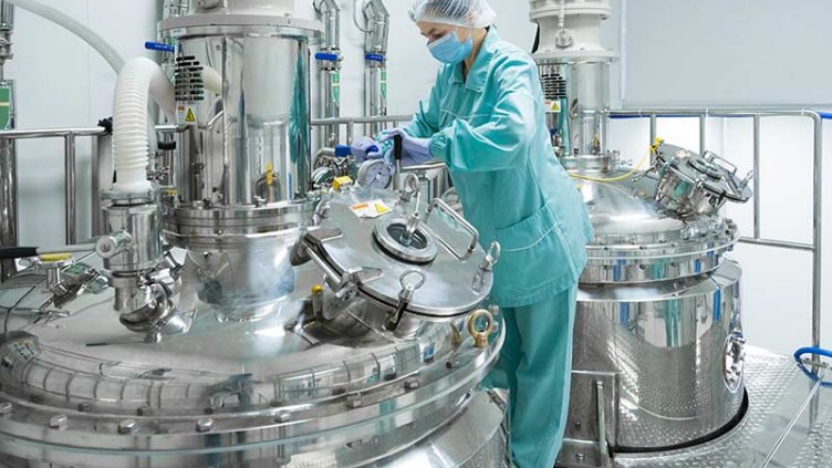 Pharmaceutical factory woman worker in protective clothing operating production line in sterile environment