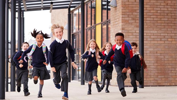 Preschool students running down a hallway while at school in the North East of England. They are laughing and having fun while their teacher follows out of focus behind them.
