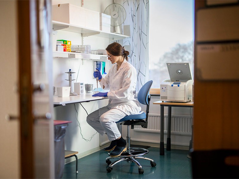 Portrait of a young woman wearing glasses and a lab coat. She is working in a life sciences lab and holding a syringe.