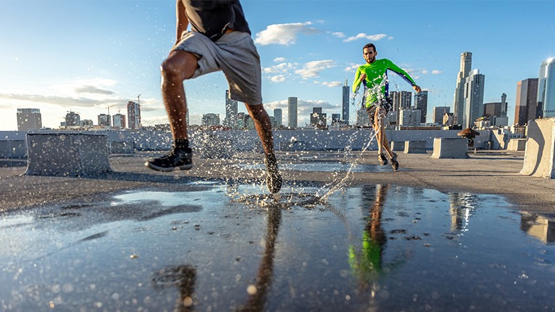 Two men jogging on a wet strech in the front of high rise buildings