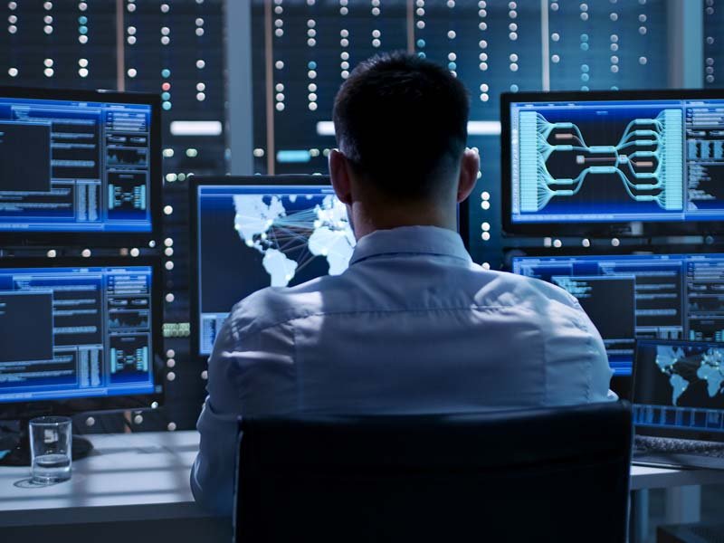 Man at computer station monitoring for cybersecurity