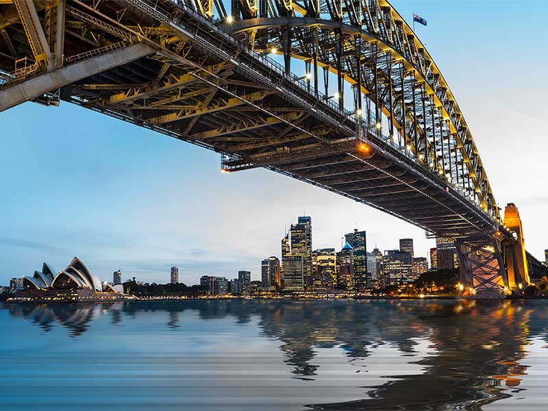 Dramatic widescreen panoramic image of the city of Sydney at sunset with bridge in foreground. Includes the Rocks, Bridge, Opera House, and a broad view of CBD and the water in the harbour
