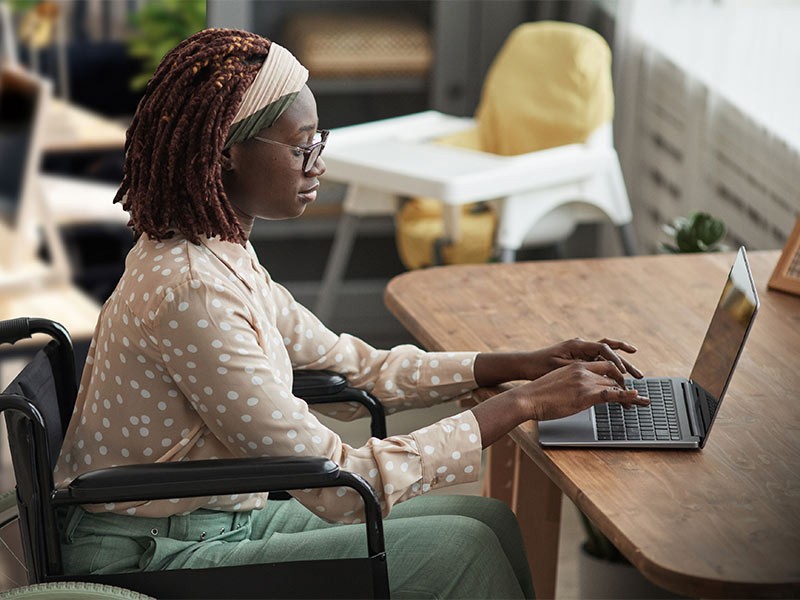 Side view of businesswoman working on laptop while sitting on wheelchair in the office