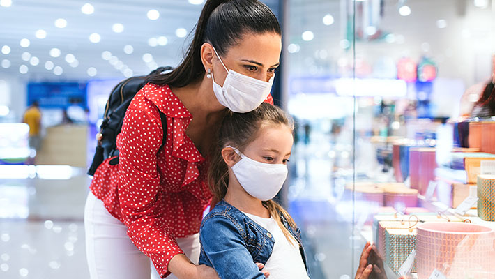 Mother and daughter with face mask standing indoors in shopping center, coronavirus concept.
