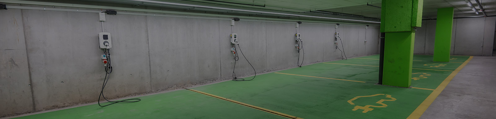 Bright, well-lit parking garage equipped with charging stations for electric cars with green and yellow painted stalls to differentiate them from other parking spaces.