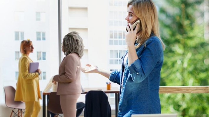 Businesswoman attending a phone call and two others having conversation with each other in office workplace