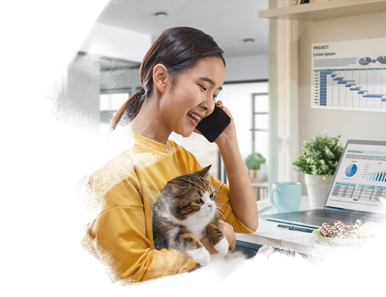 Young woman holding a cat and talking on the phone while sitting at her home work desk.